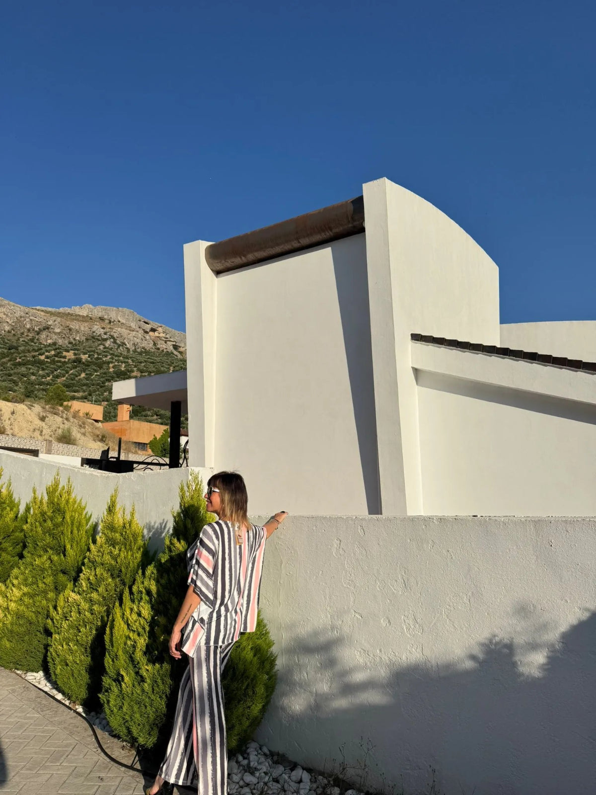 Parte trasera del conjunto de blusa más pantalón con estampado a rayas verticales en tonos claros (negro, gris, blanco y rosa)